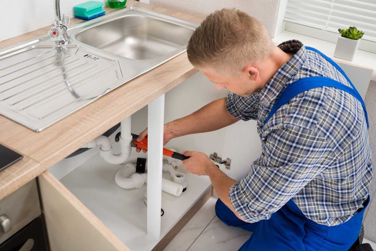 Plumber repairing pipes under a kitchen sink with a wrench